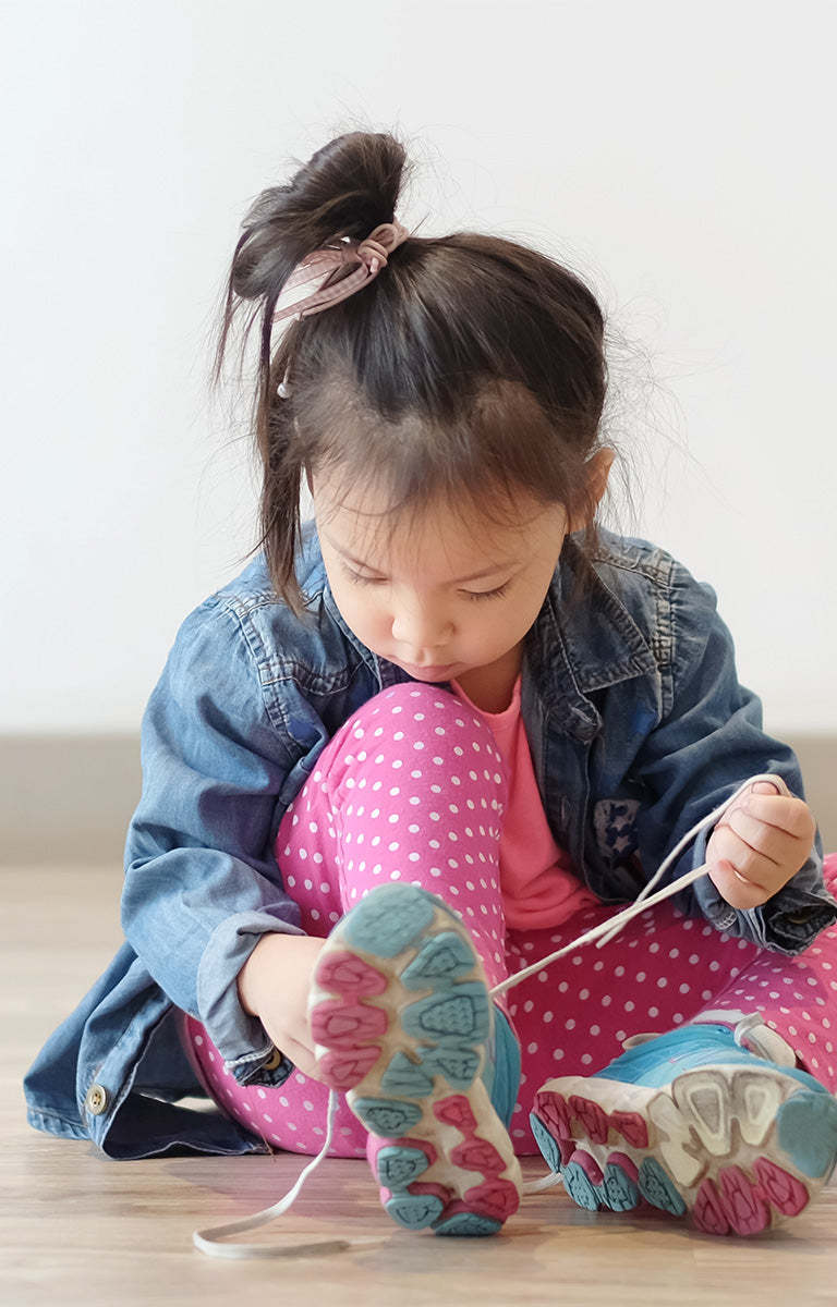 Niña pequeña poniendose los zapatos.